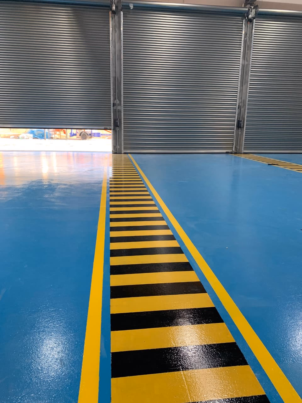 2MIC : Allée piétonne bordée de bandes noires et jaunes sur époxy bleu