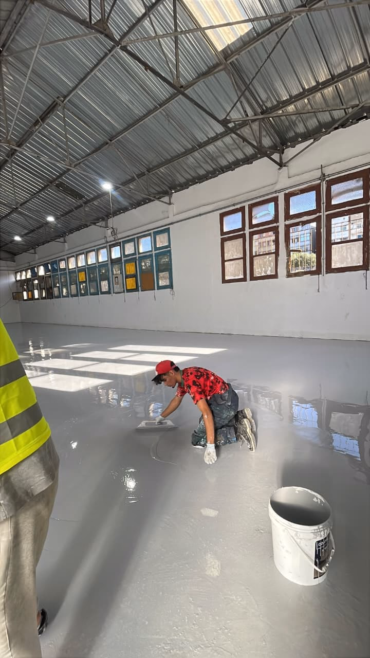 Applicateur lissant la résine époxy à la truelle dans une salle lumineuse